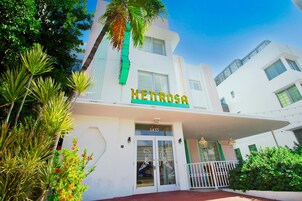 Un hotel llamado 'HENROSA' con fachada blanca, detalles en verde y un balcón con barandilla.