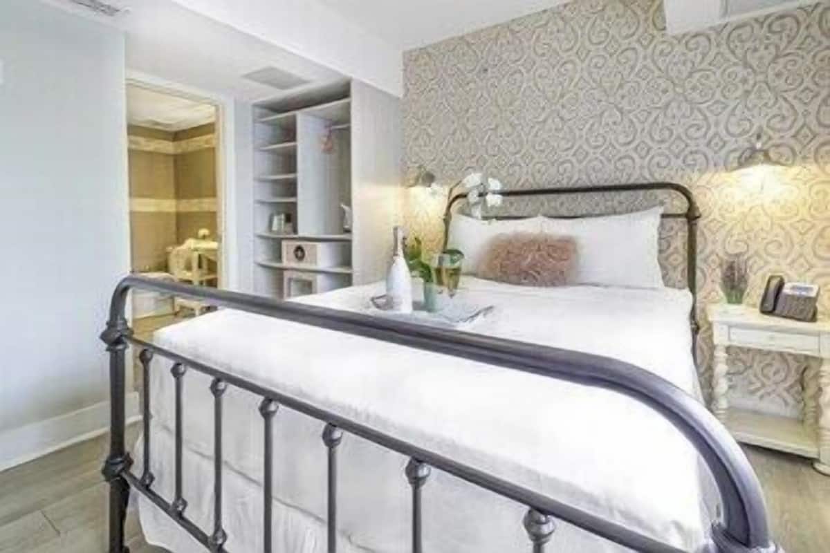 A bedroom with a metal bed frame, a bedside table with a lamp, a nightstand, and a built-in wardrobe.