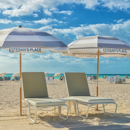 Two beach chairs under umbrellas labeled "Esteban's Place" with a beach and ocean in the background.
