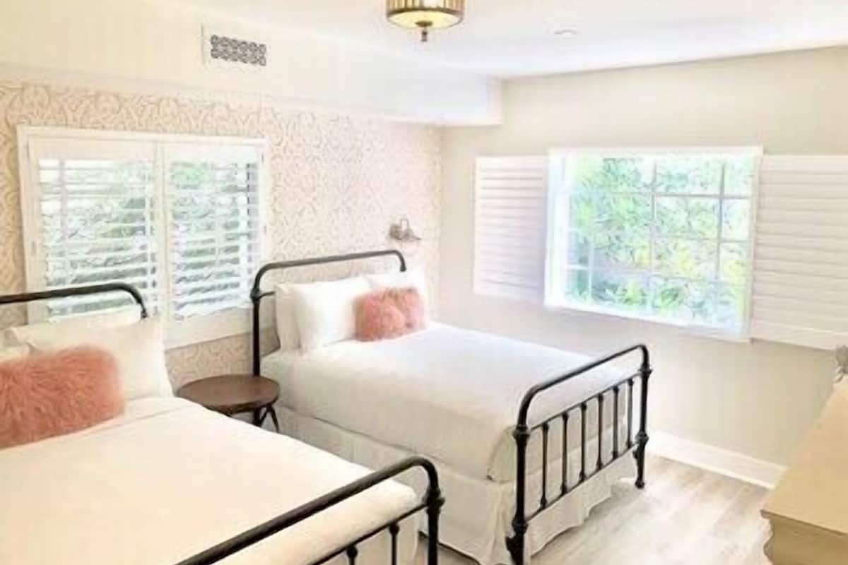 A bedroom with two beds, a window with blinds, a ceiling light fixture, and a patterned wall.