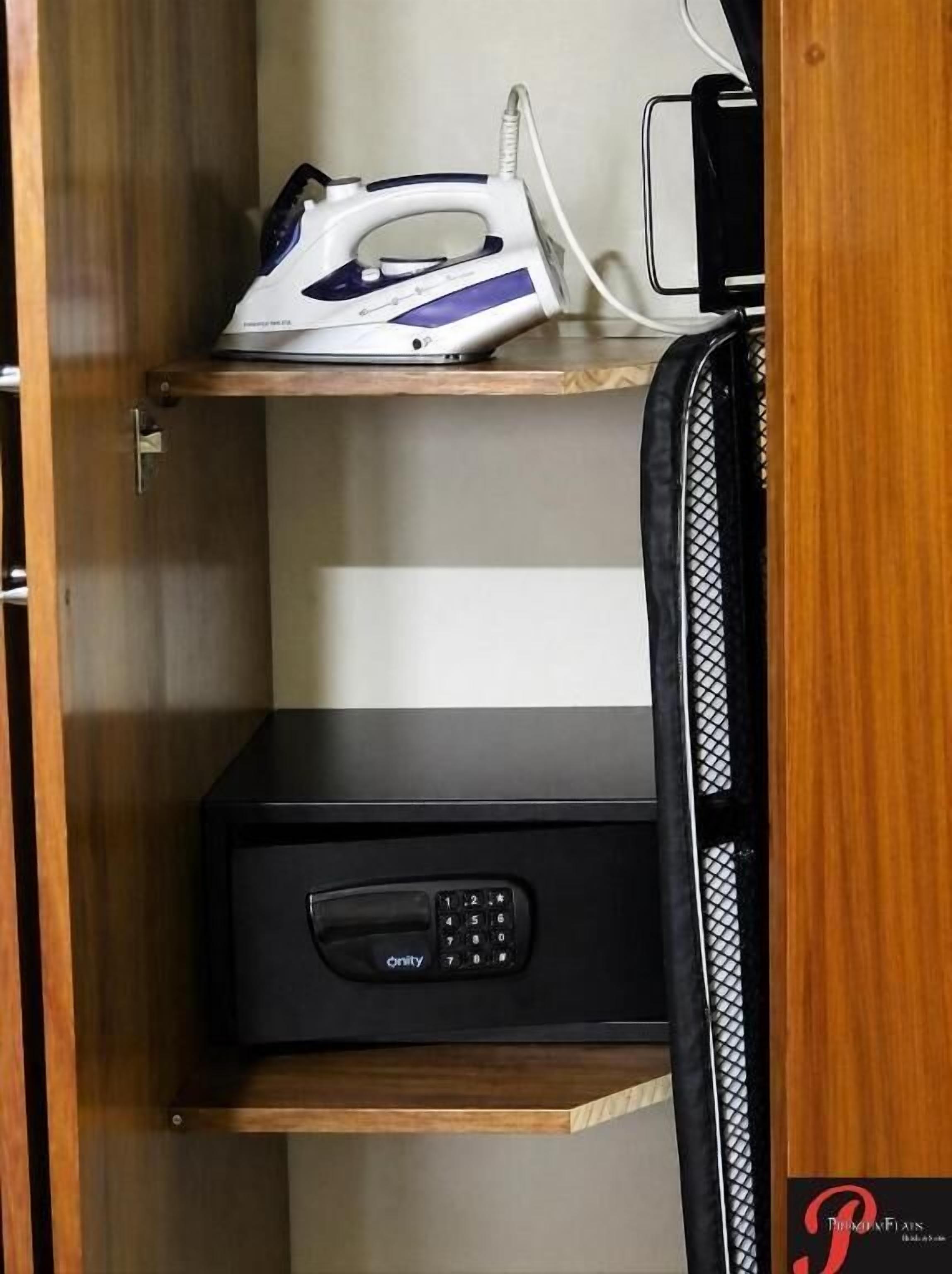 Un armario de madera con un estante que contiene un planchador y un dispositivo electrónico negro.