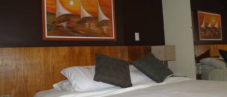 A hotel room with a large bed, two patterned pillows, a wooden headboard, a nightstand with a telephone, and two framed paintings on the wall.