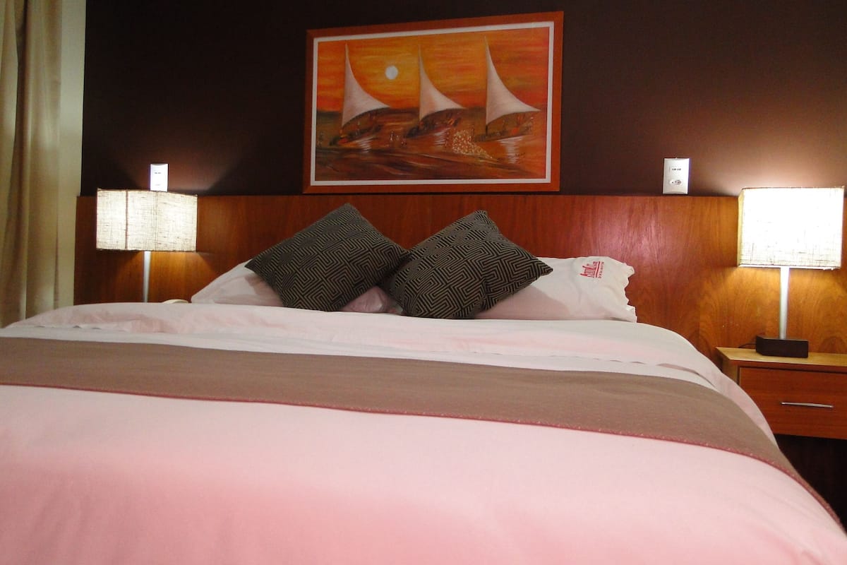 Ein Hotelzimmer mit einem Bett, zwei Nachttischlampen, einem Segelbootgemälde und einem hölzernen Kopfstück.