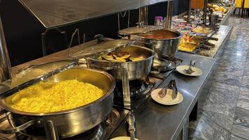 Montaje de bufé con diferentes alimentos en ollas de metal grandes, incluyendo lo que parecen huevos revueltos y un guiso.