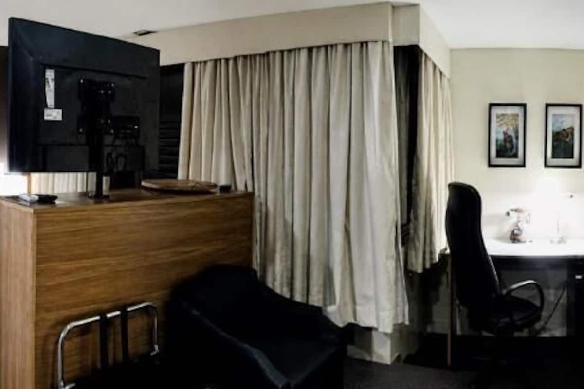 Ein Hotelzimmer mit Bett, Schreibtisch, Stuhl, einer Kaffeemaschine und Vorhängen.