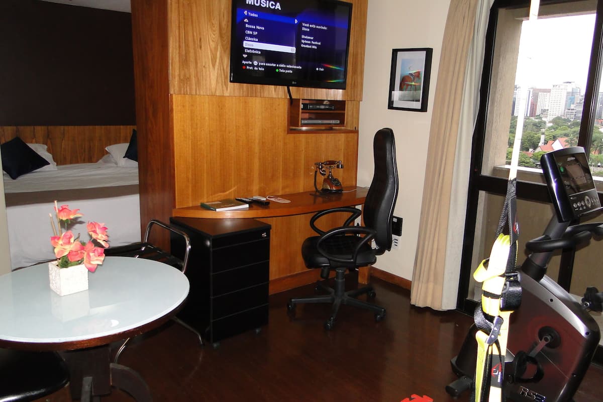 Ein Hotelzimmer mit Bett, Schreibtisch mit Computer, Stuhl, Wandfernseher und Fenster mit Stadtblick.