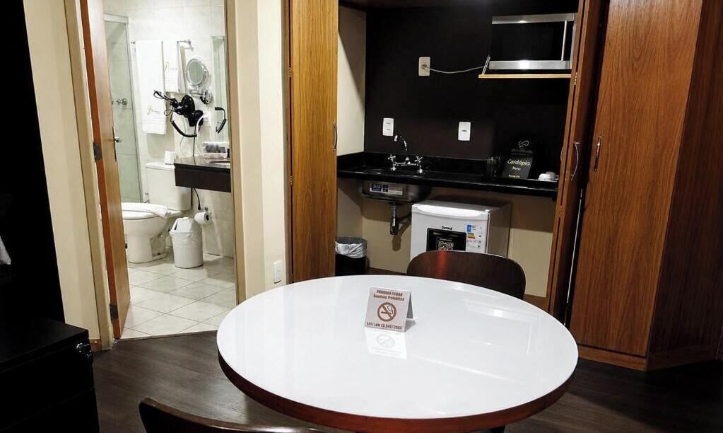 A small room with a round table, a black countertop with a sink, a microwave, and a small refrigerator.