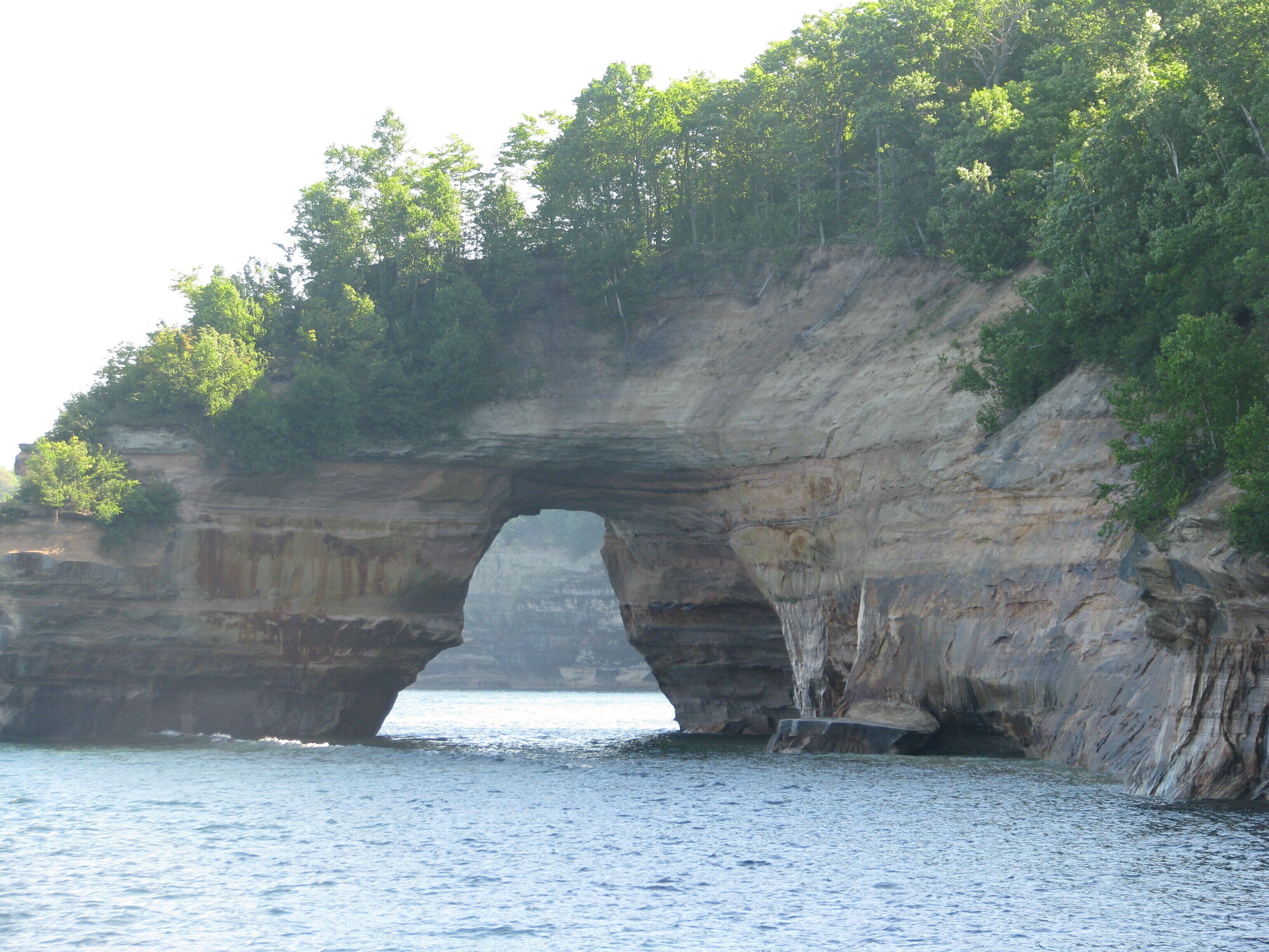 Un arco natural de roca sobre un cuerpo de agua, rodeado de vegetación.