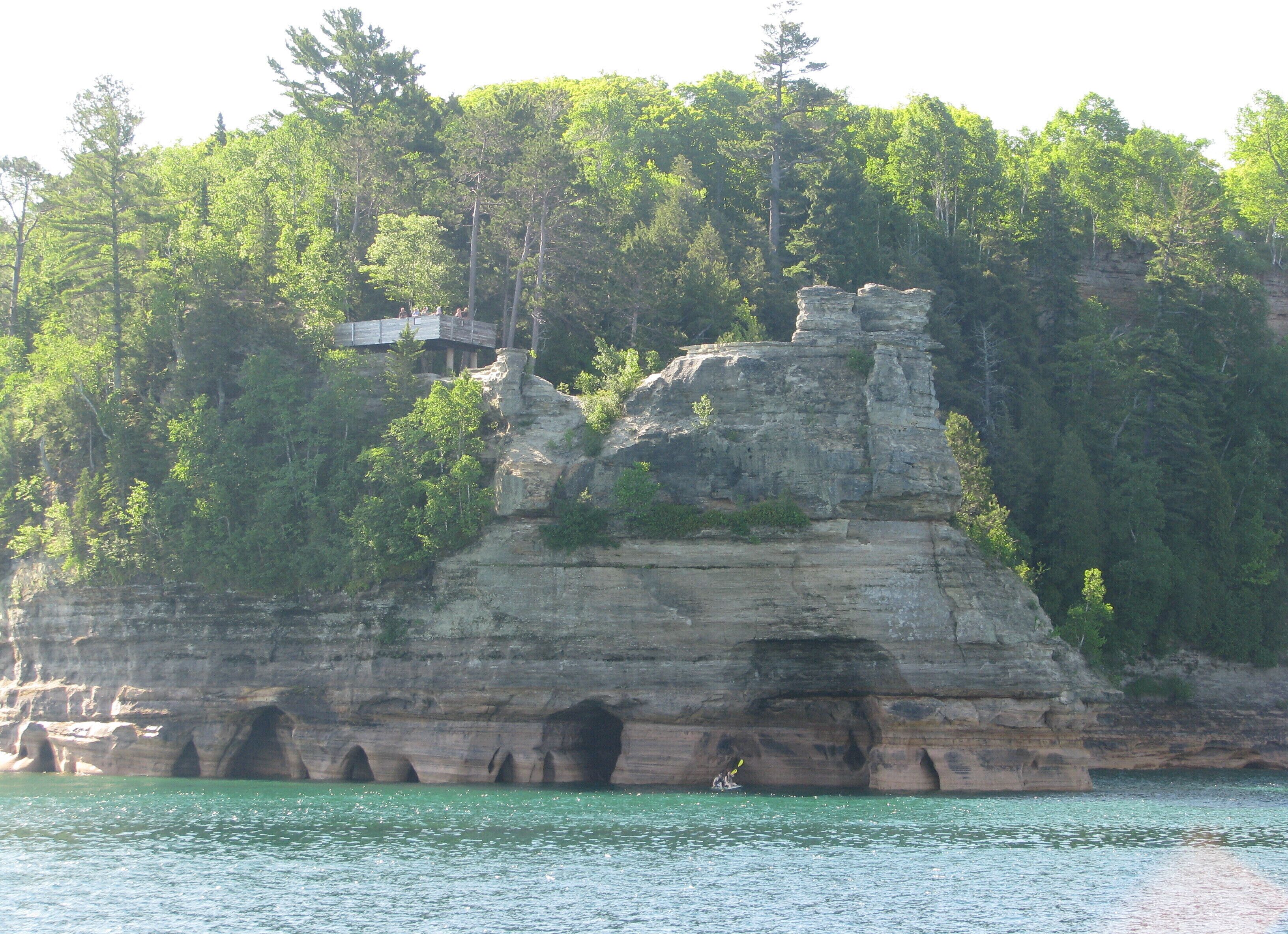 A natural rock formation with a small building on top, surrounded by dense forest.