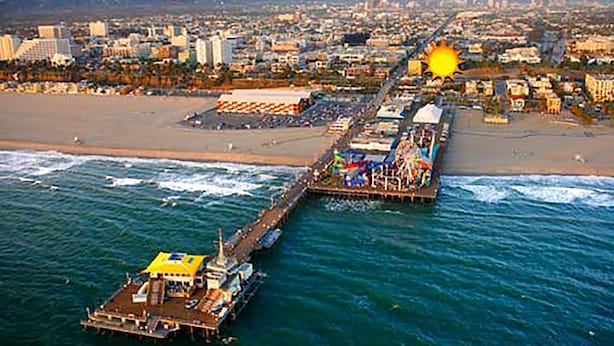 An aerial view of a coastal city with a pier extending into the ocean, featuring a large Ferris wheel and a ship docked at the pier's end. - Ocean Lodge Santa Monica Beach Hotel (Santa Monica)
