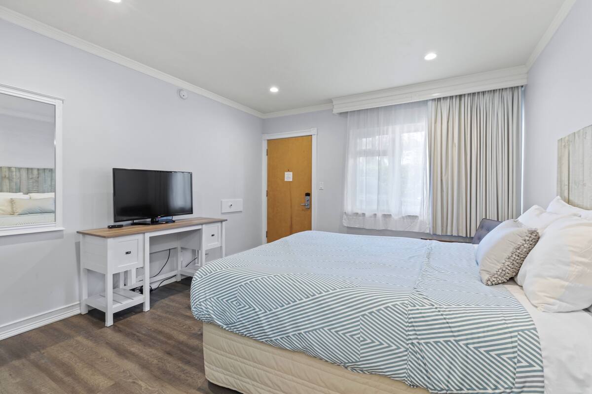 Una habitación de hotel moderna con una cama grande, un televisor sobre un escritorio de madera y una ventana con cortinas.