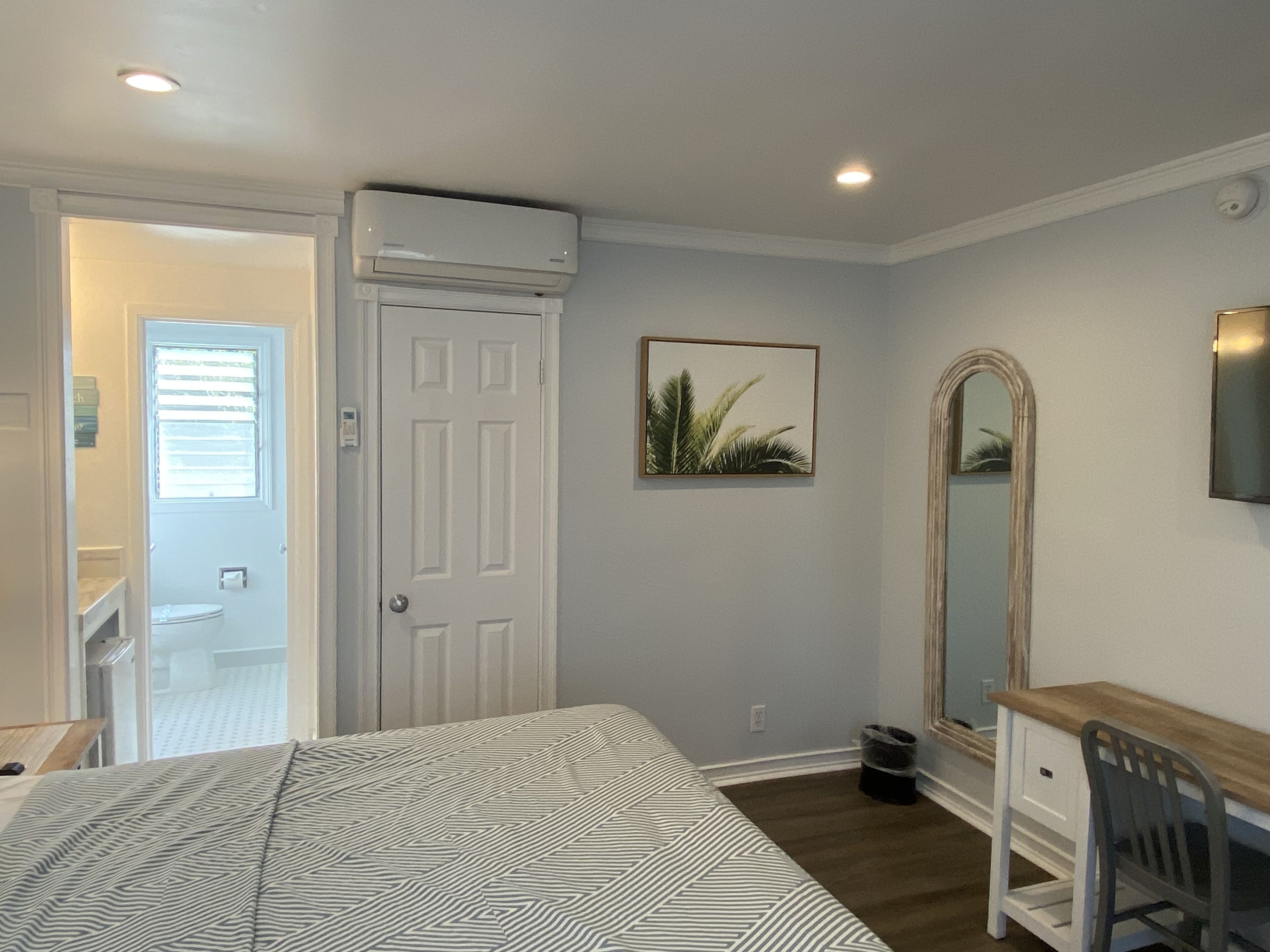 Une chambre à coucher comprenant un lit, une commode, un miroir et une porte donnant sur une salle de bain.