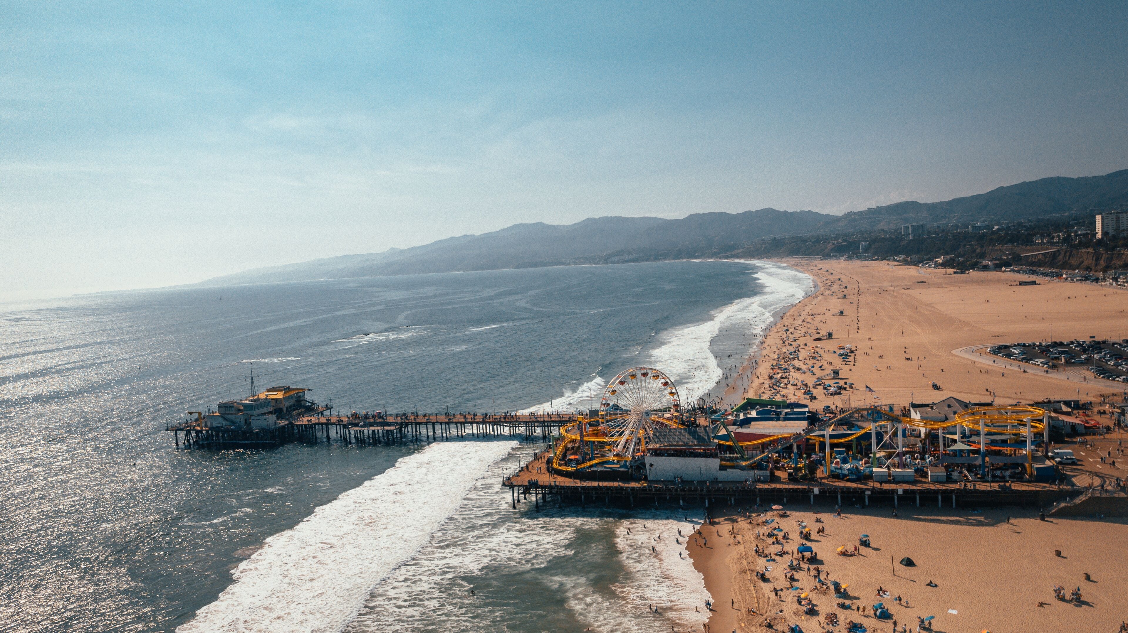 A pier extending into the ocean with a beach and mountains in the background.
