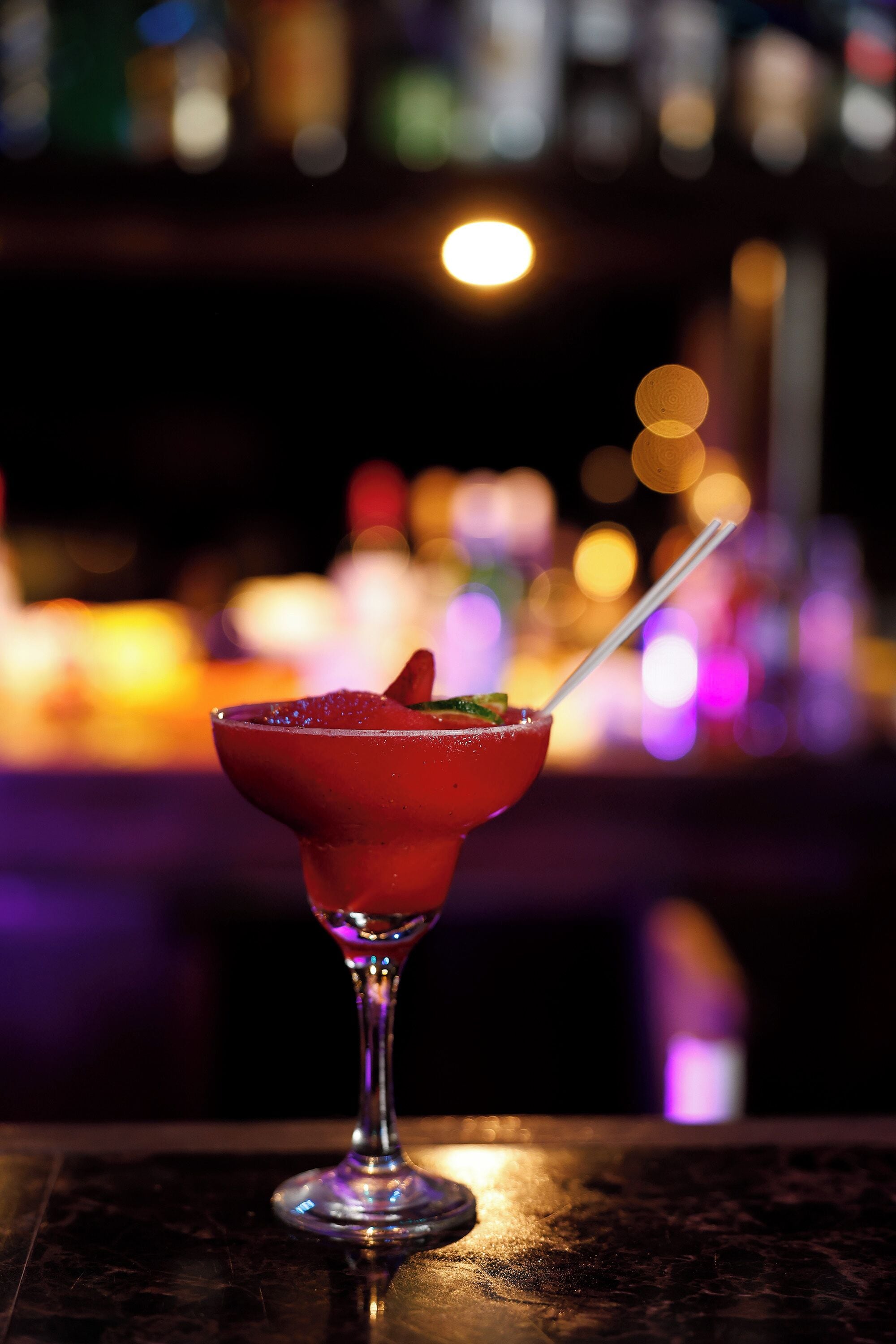 A cocktail in a glass with a straw, set against a blurred background of lights.