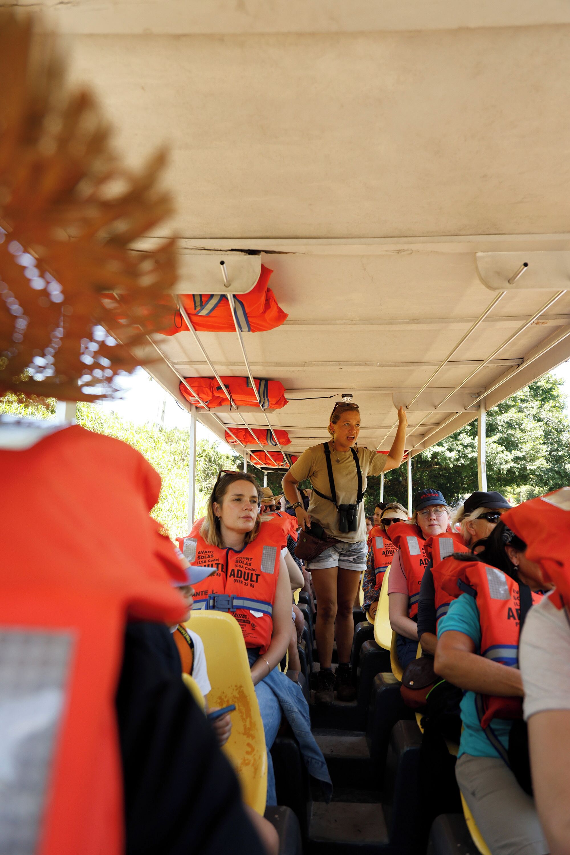 A group of people in orange life jackets seated in a covered bus.