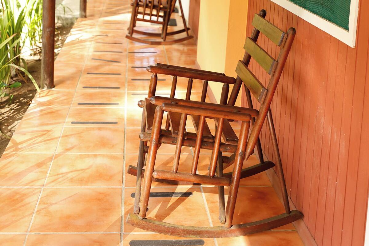 Un pasillo cubierto con mecedoras de madera, suelo de baldosas y persianas verdes.