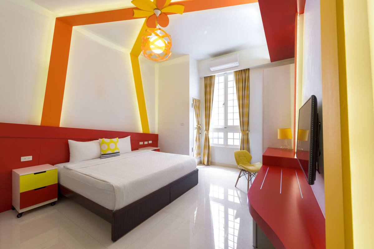 A modern hotel room with a large bed, a desk, a chair, and a TV.