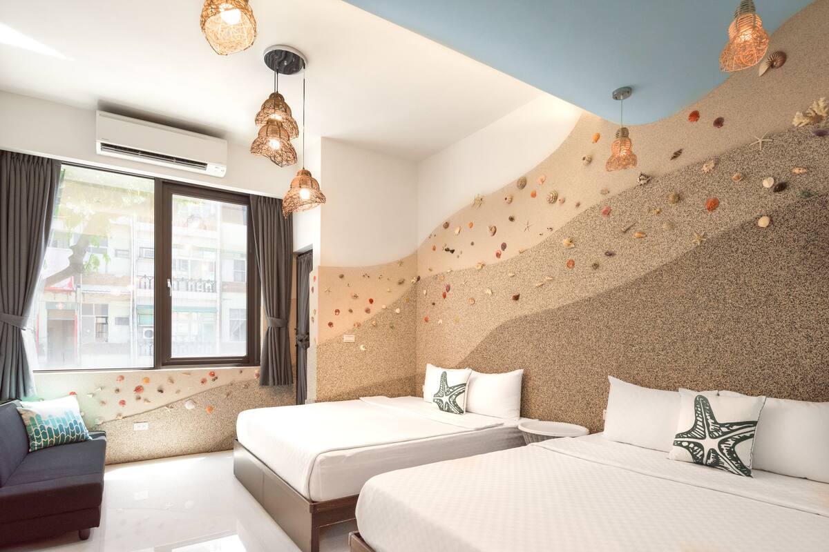 A hotel room with two beds, a sofa, and a large window.