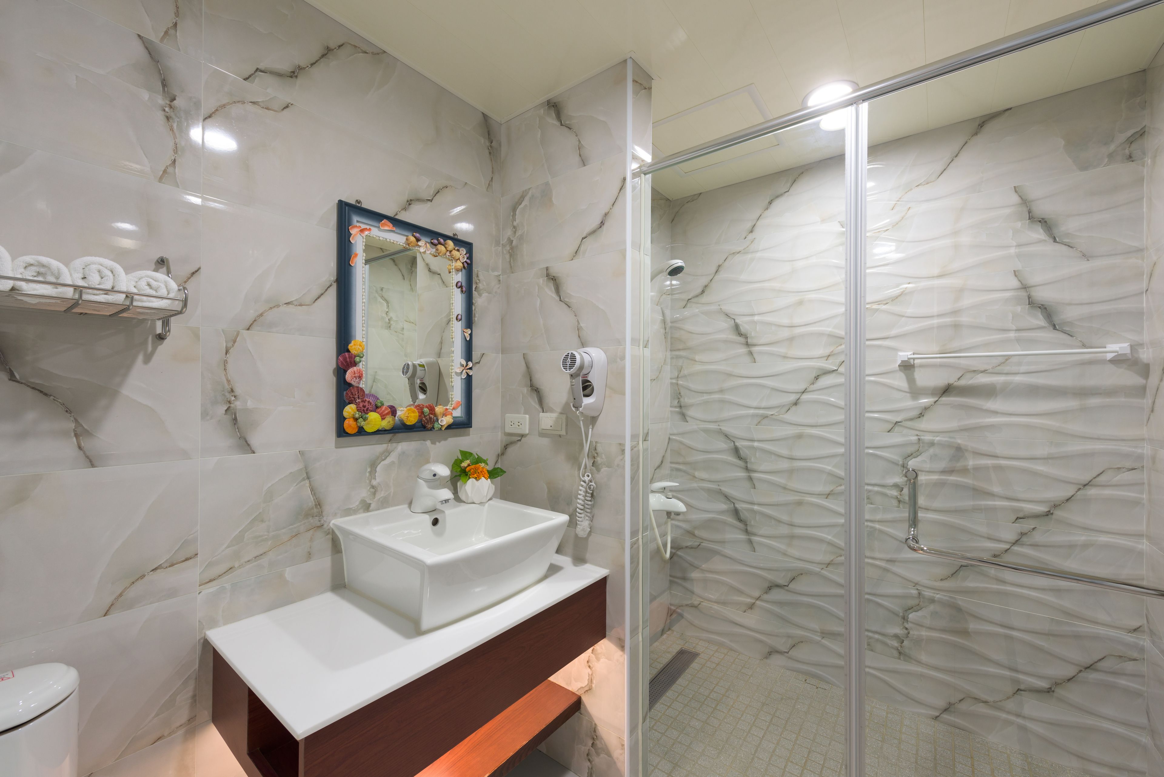 A bathroom with a marble wall, a sink, a mirror, and a shower.