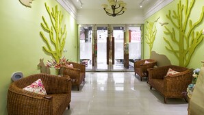 A lobby with wicker sofas, a chandelier, and green wall art. - Luna's House (Kaohsiung)
