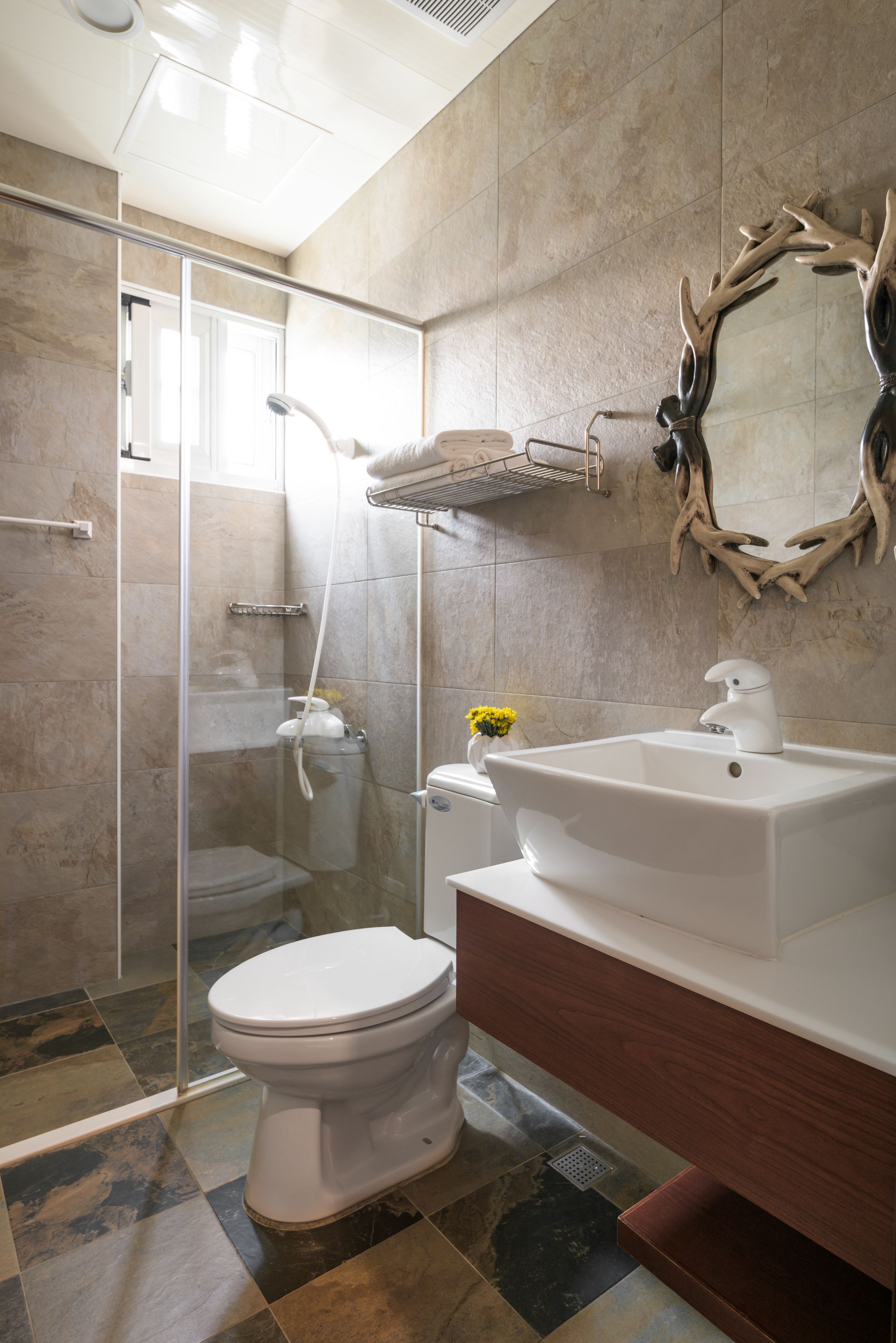 A modern bathroom with a glass shower enclosure, a white toilet, a sink with a mirror, and a decorative antler mirror.