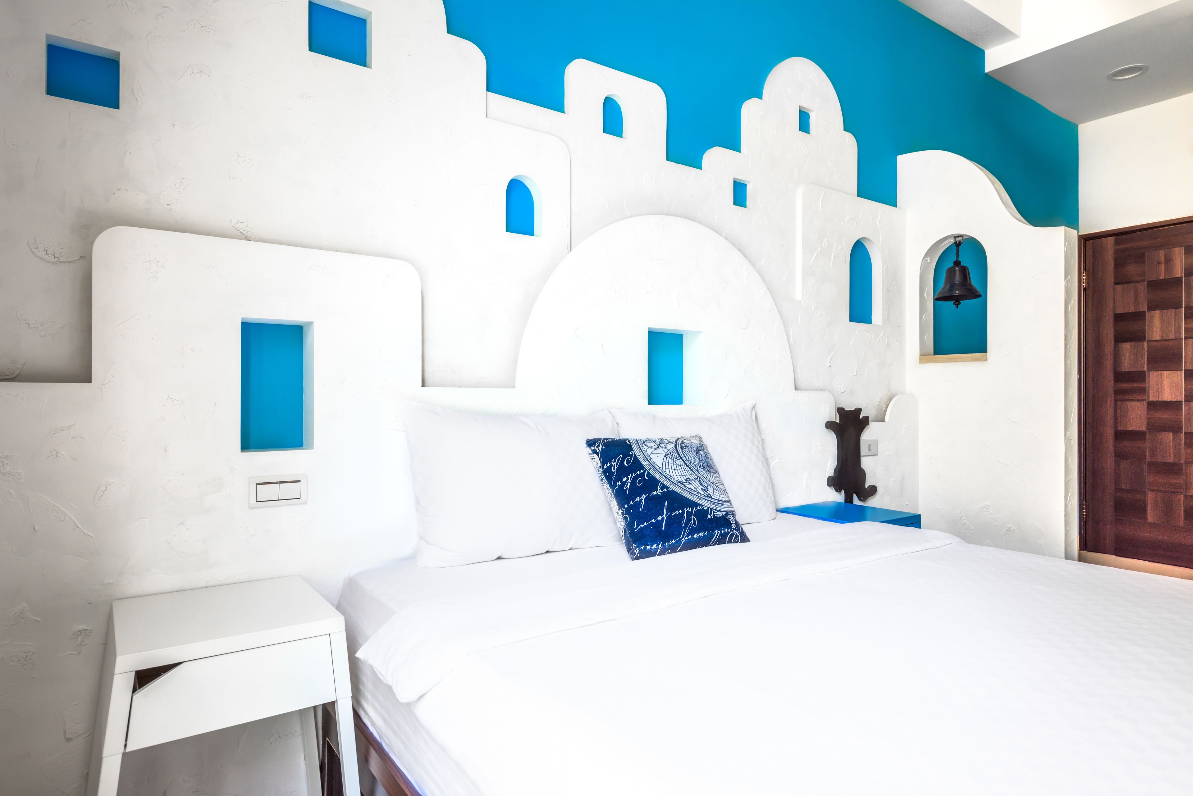 A bedroom with a white bed, blue accent pillows, and a white nightstand.