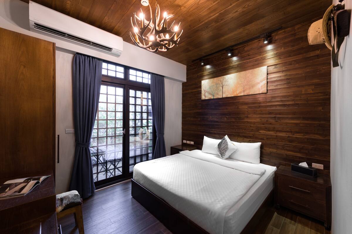 A bedroom with a large bed, wooden walls, a chandelier, and a sliding glass door leading to an outdoor area.