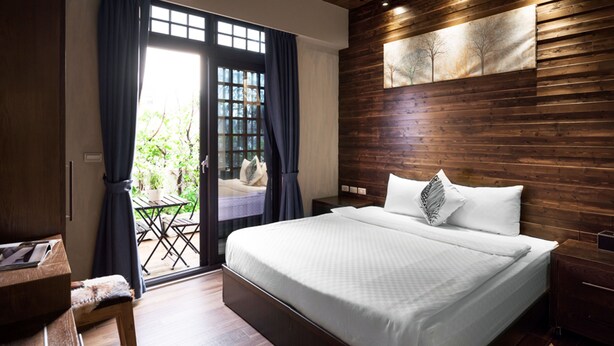 A bedroom with a large bed, wooden paneling on the walls, a window with curtains, and a view of the outdoors. - Luna's House (Kaohsiung)