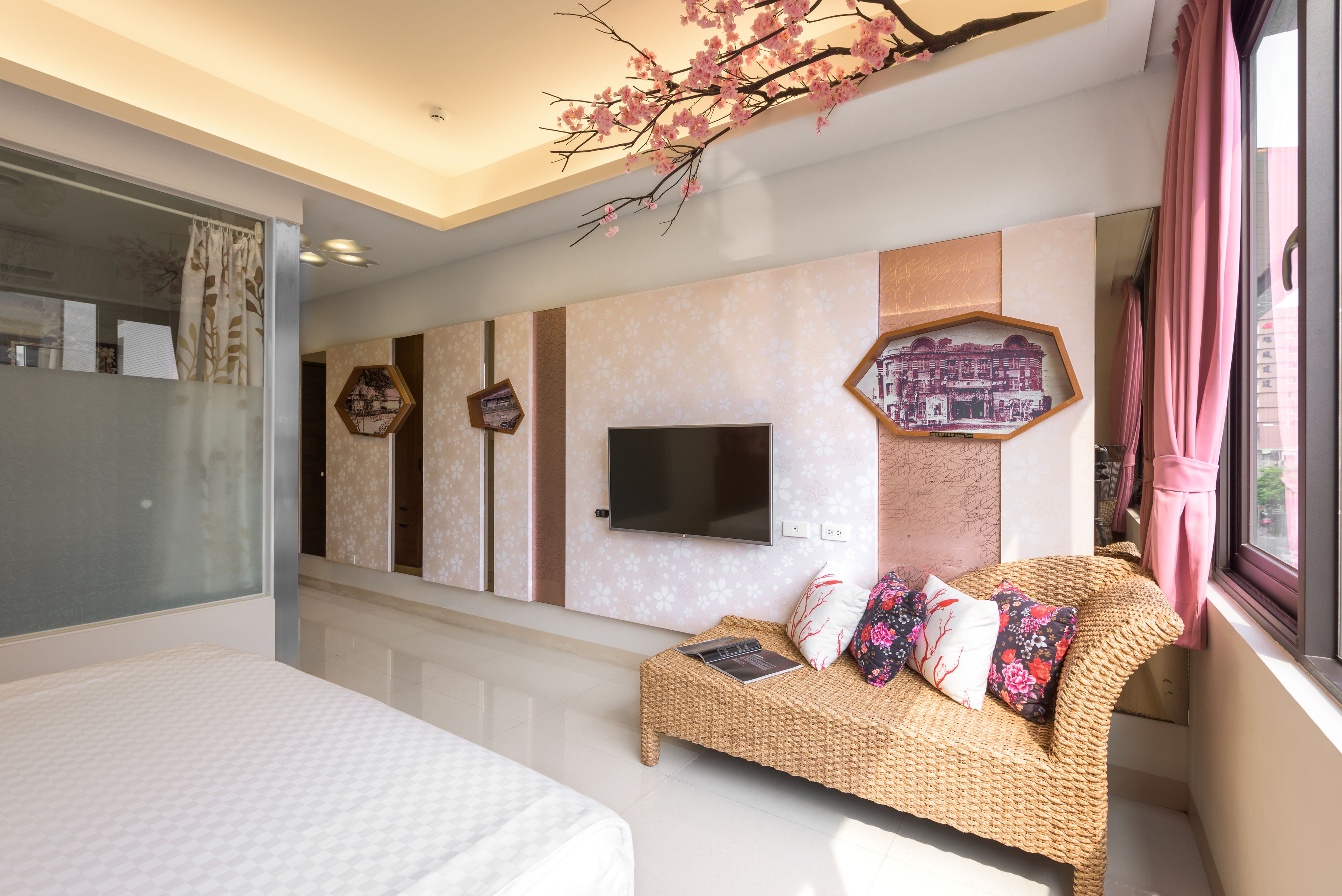 A modern bedroom with a large bed, a wicker sofa, a flat-screen TV, and decorative wall art.