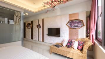 A modern bedroom with a large bed, a wicker sofa, a flat-screen TV, and decorative wall art.