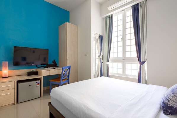 Habitación de hotel con cama, escritorio con computadora, televisor y un refrigerador pequeño.