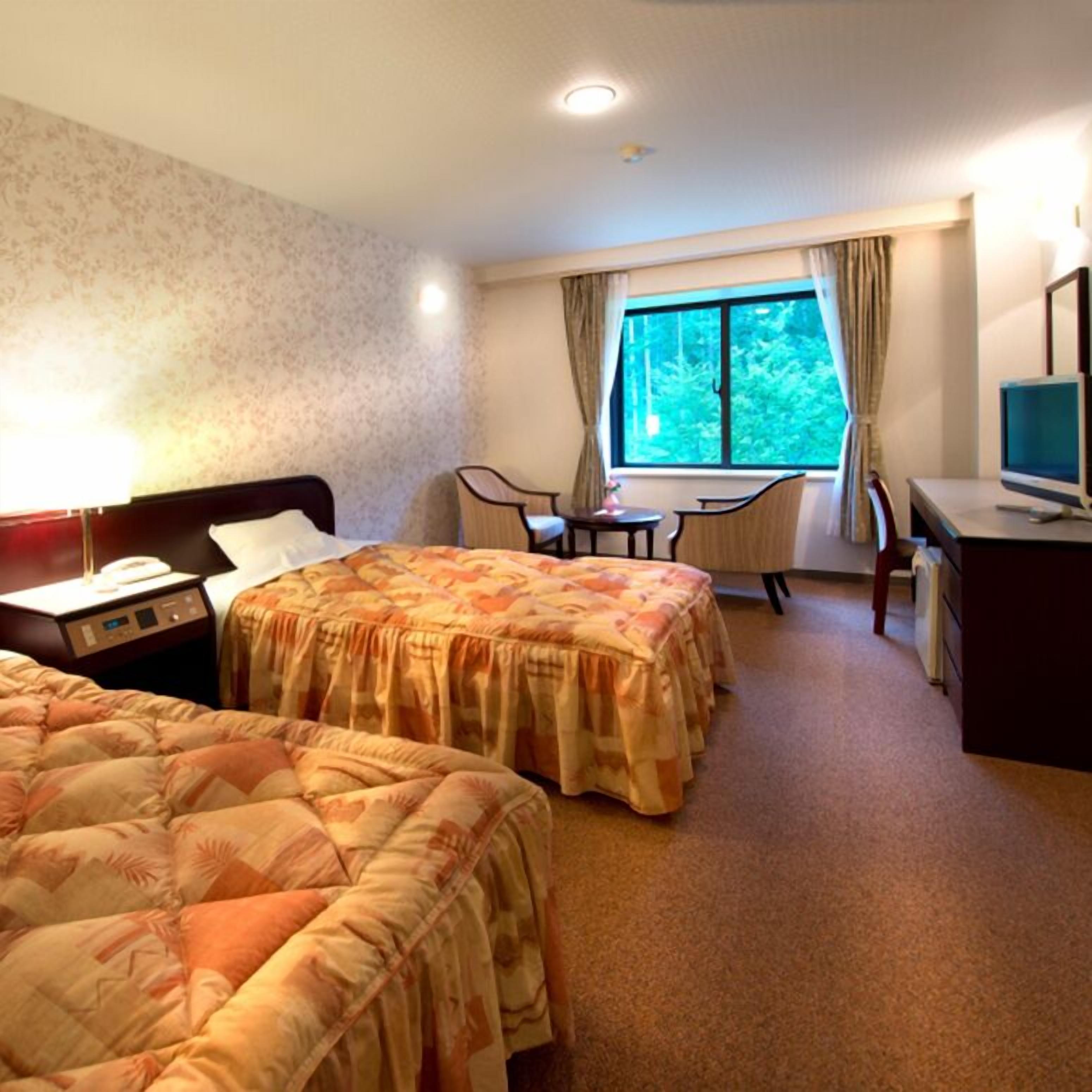 A hotel room with two beds, a desk, a chair, a TV, and a window with a view of trees.