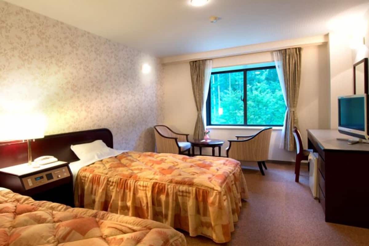 Habitación de hotel con dos camas, un escritorio, una silla, un televisor y una ventana con vista a árboles.