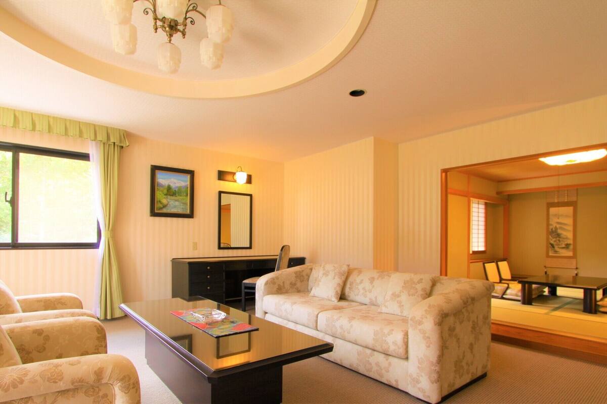 A hotel room with a sofa, armchairs, a coffee table, a desk, and a painting on the wall.