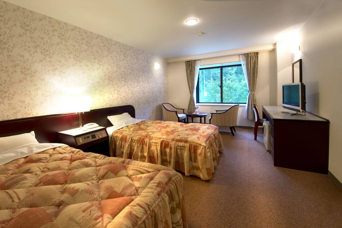 A hotel room with two beds, a desk, a chair, a TV, and a window with curtains.