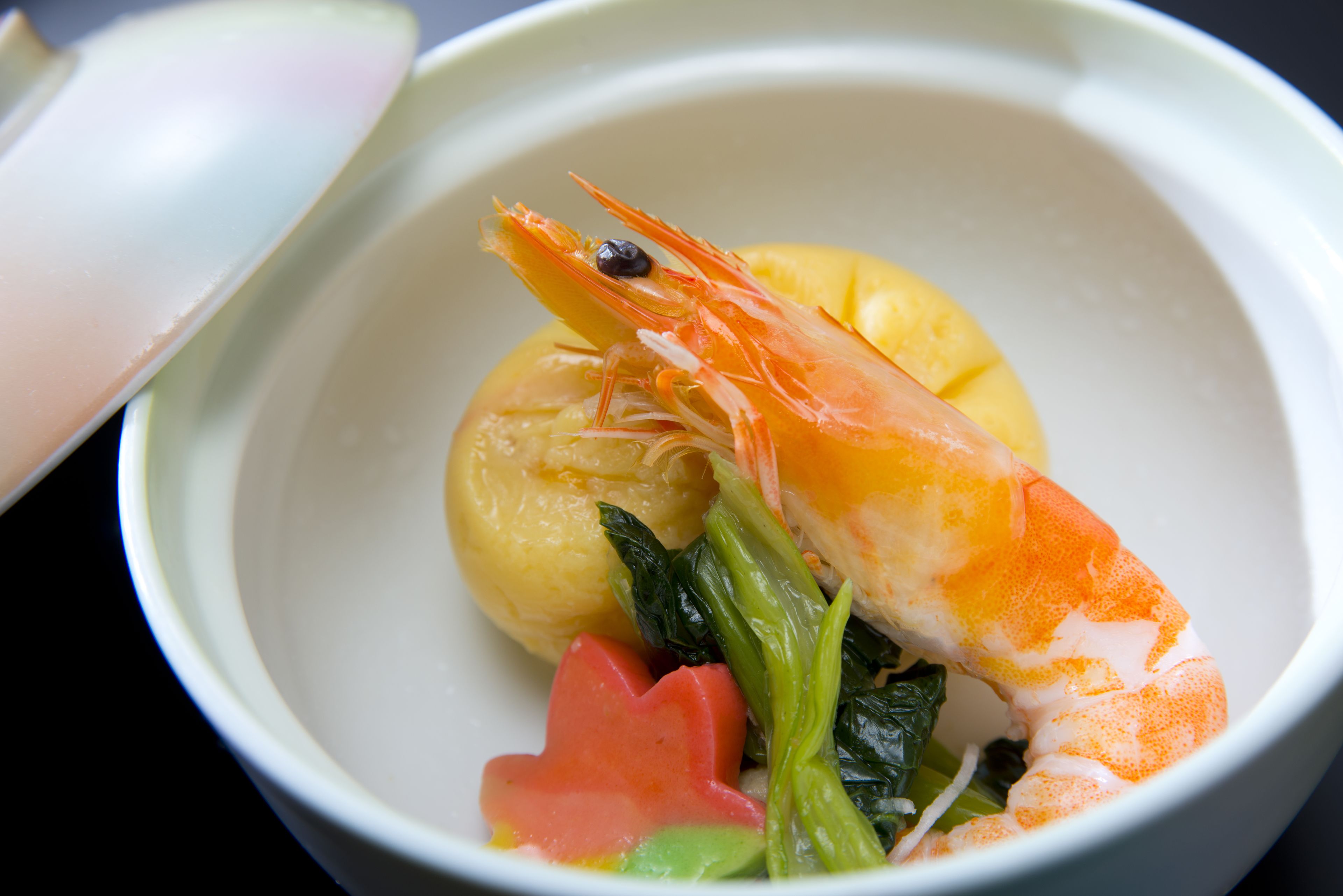 A bowl of food with a shrimp, a slice of lemon, and some greens.