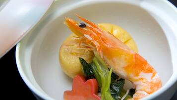 A bowl of food with a shrimp, a slice of lemon, and some greens.