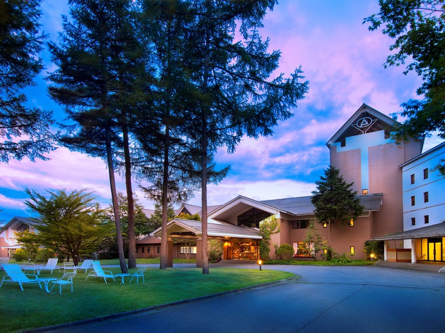 A hotel with a modern design, featuring a large entrance, outdoor seating area, and a well-maintained lawn.
