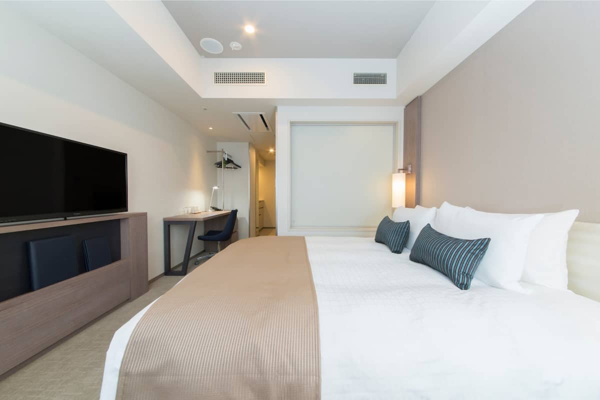 A modern hotel room with a large bed, a flat-screen TV, a desk with a chair, and a walk-in closet.