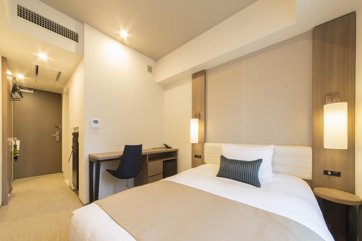 A hotel room with a large bed, a desk, a chair, and a small table.