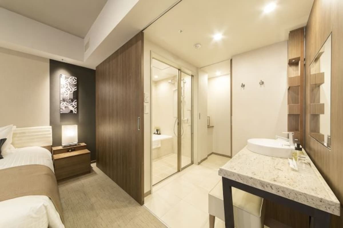 A modern hotel room with a bed, bedside table, nightstand, and a large mirror.