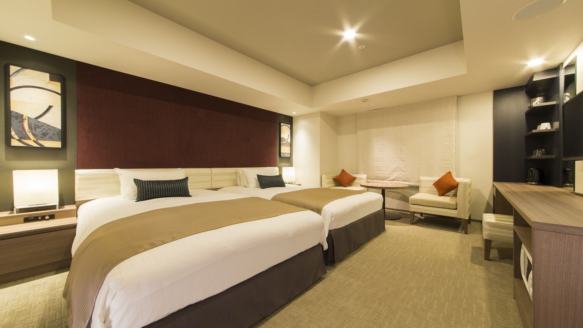 A hotel room with two beds, a desk, a chair, and a small table.