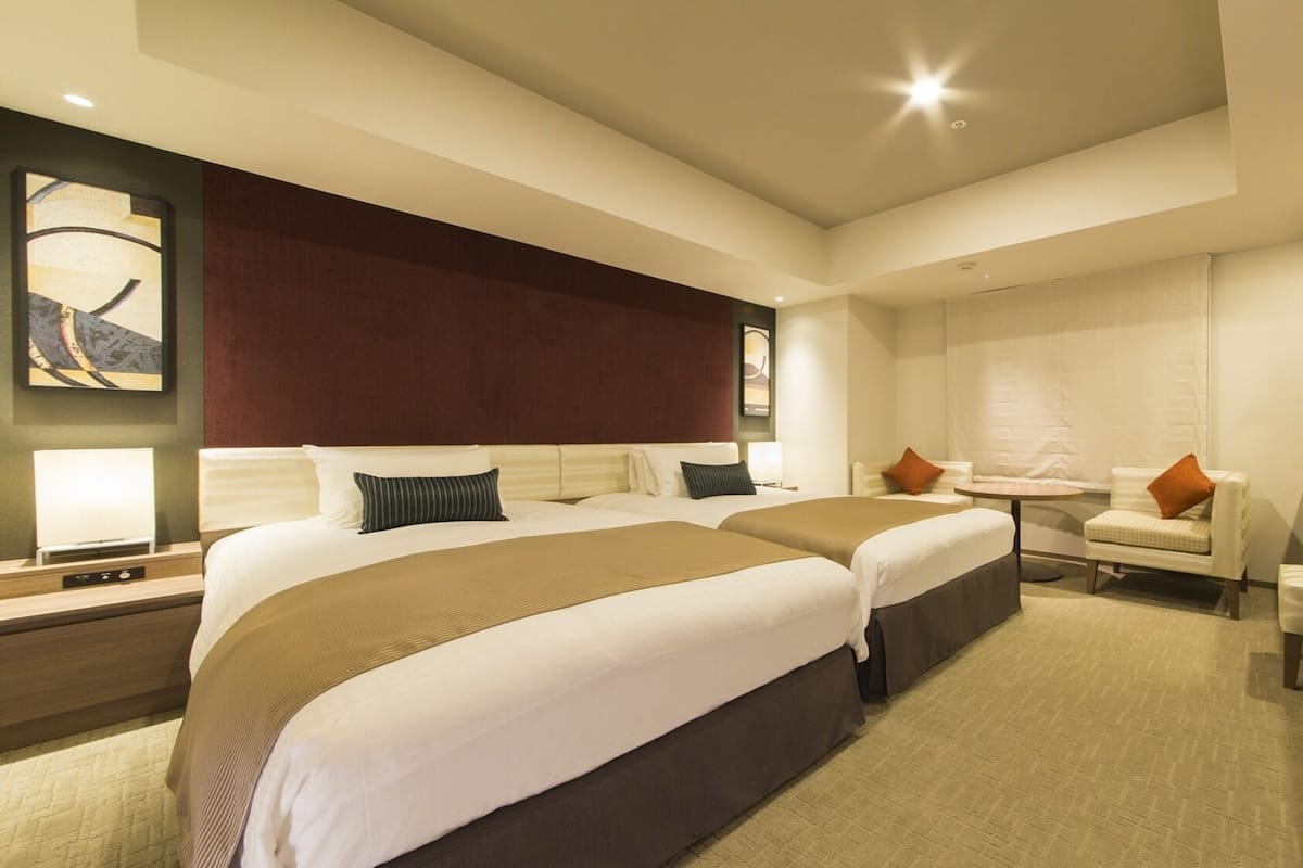 A hotel room with two beds, a desk, a chair, and a small table.