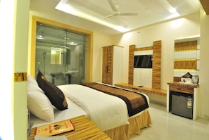 A hotel room with a bed, bedside table, a small refrigerator, a mirror, and a shower area.