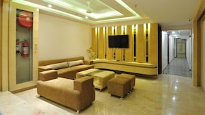 A modern living room with a sectional sofa, ottomans, a glass coffee table, and a flat-screen TV mounted on a wooden panel wall.