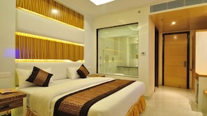 A modern hotel room with a large bed, a glass shower enclosure, and a wooden door.