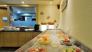 A buffet area with various dishes on ice, a kitchen in the background, and a wall with framed pictures.