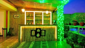 A bar area with a bamboo wall, shelves with beverages, and green ambient lighting.