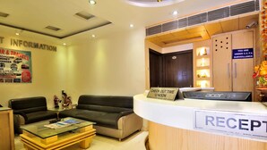 A reception area with a glass-top desk, a sign indicating check-out time, a sofa, and a wall with information posters. - Hotel Sonu Dx New Delhi Railway Station (New Delhi)