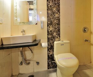 A bathroom with a white sink, mirror, toilet, and a wall with a floral tile pattern. - Hotel Sonu Dx New Delhi Railway Station (New Delhi)